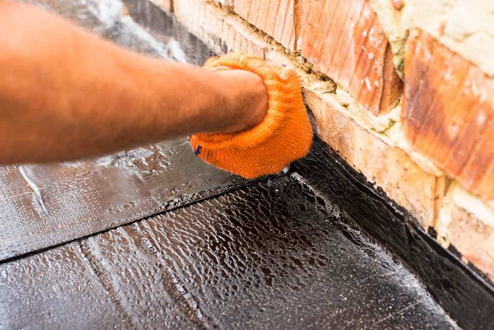 Hand wearing orange glove repairing rubber roof near section of brick.