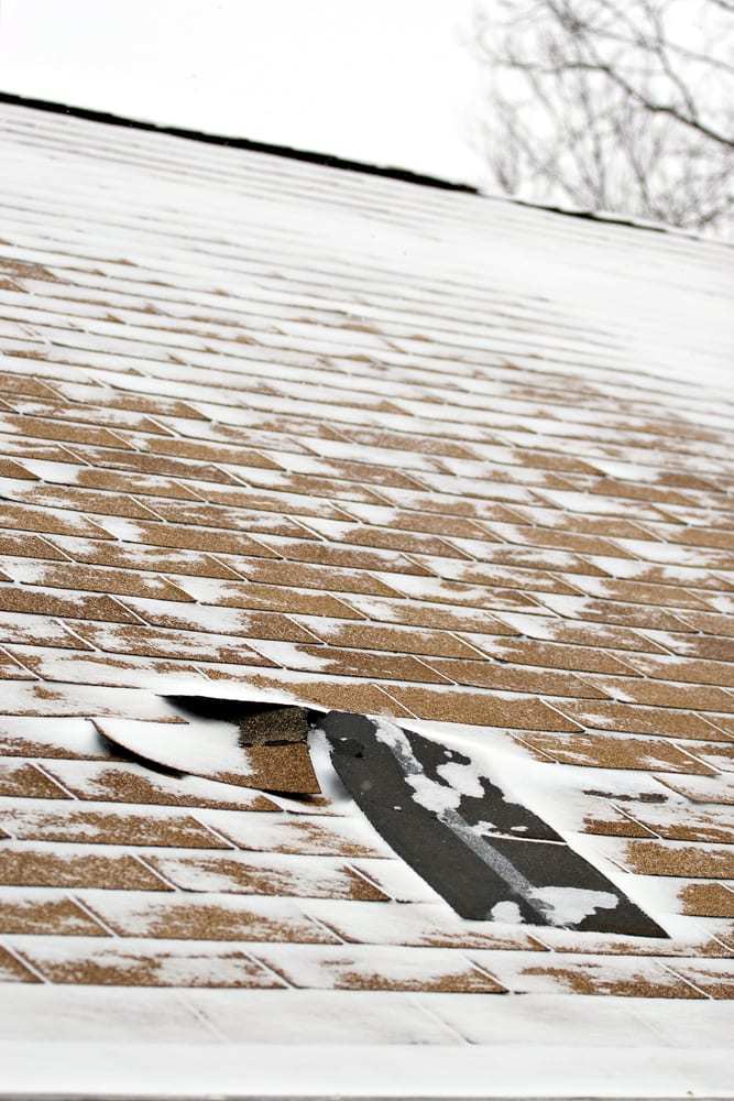 Shingles falling off roof that is topped with dusting of snow