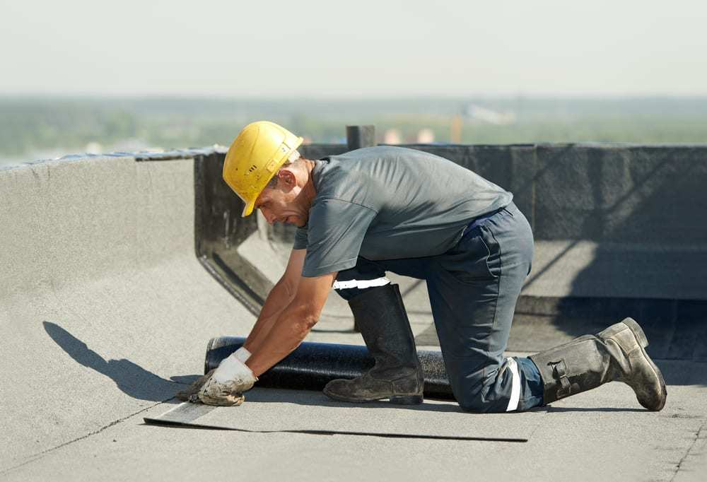 Roofer applying roofing felt to flat roof